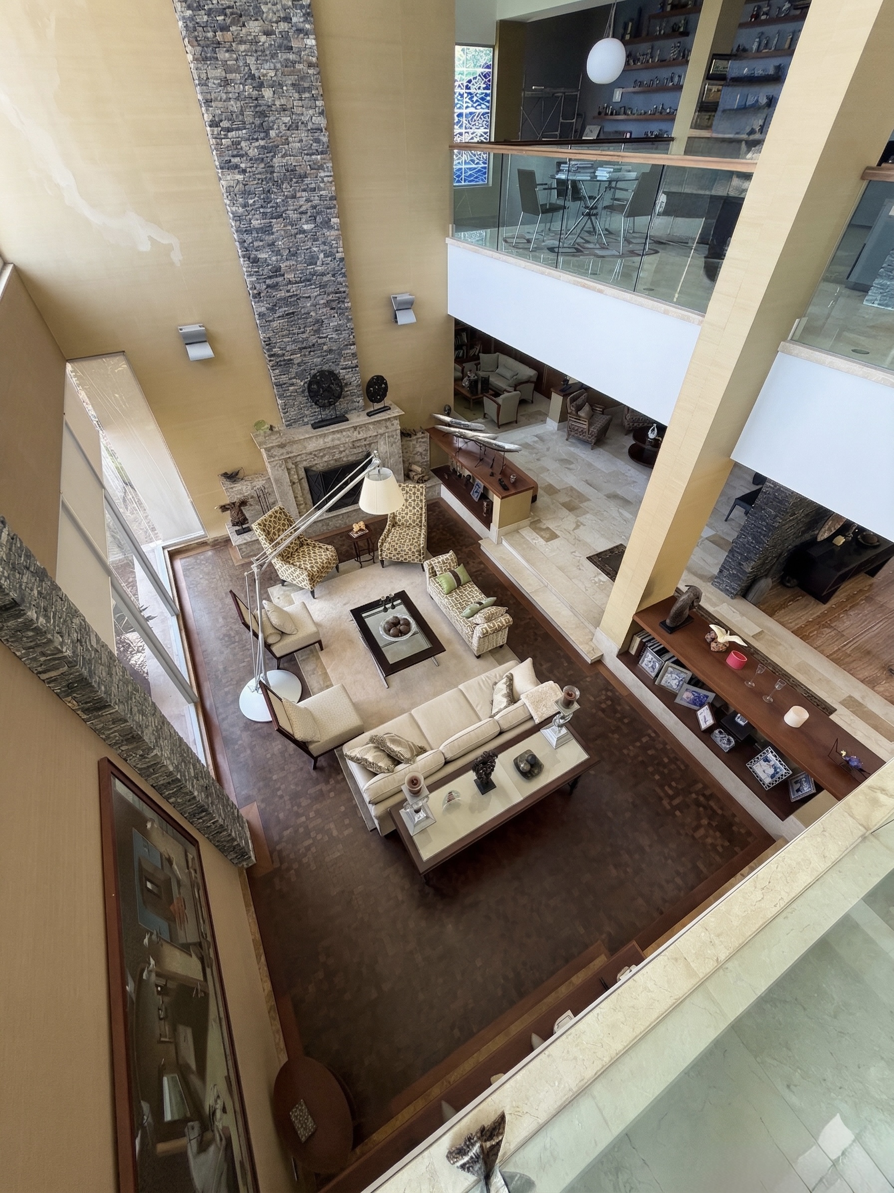 Aerial view of grand double-height living room with natural stone fireplace and panoramic mezzanine, La Trinidad estate Caracas